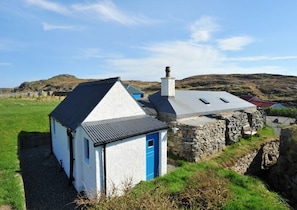 Un petit bâtiment blanc avec une porte bleue, une cheminée en pierre et un toit en pente.