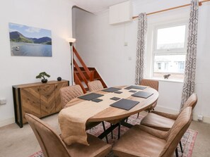 Un coin repas comprenant une table en bois, des chaises rembourrées, un buffet en bois, un tableau et un escalier.