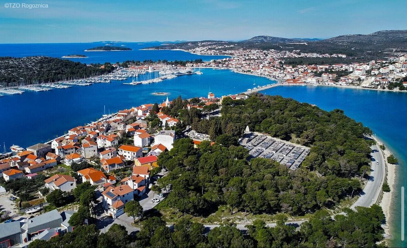 An aerial view of a coastal town with a marina, dense residential area, and a curved coastline.