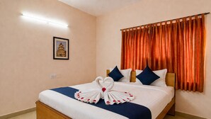 Ein Hotelzimmer mit einem ordentlich bezogenen Bett, einem gerahmten Bild an der Wand und einem Fenster mit orangefarbenen Vorhängen.
