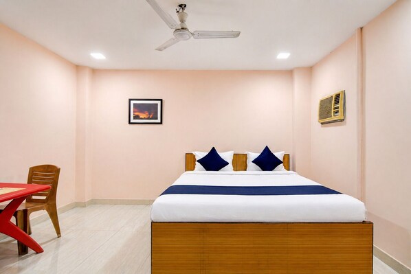 A hotel room with a bed, a ceiling fan, a picture on the wall, and a table with a chair. - Hotel Blue Bird (Barakpur)
