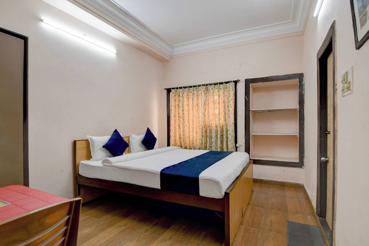 A bedroom with a bed, a desk, a chair, a shelf, and a door.