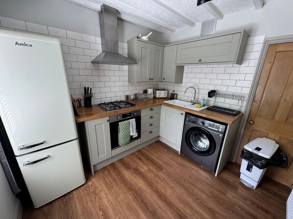 Una cocina compacta con un refrigerador blanco, estufa, lavamanos y lavadora.
