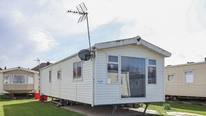 Una casa móvil con antena parabólica, un pequeño porche y una ventana decorada con un corazón.