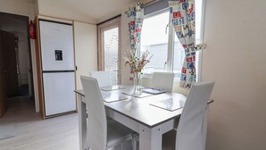 Una cocina compacta con refrigerador, una mesa de comedor con sillas y una ventana con cortinas estampadas.
