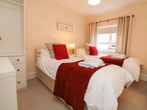 A hotel room with two beds, a white dresser, a window with curtains, and a wall-mounted picture.