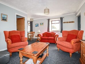 A room with two red armchairs, a wooden coffee table, a dining table with chairs, and a window with curtains.