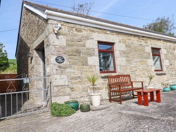 A stone cottage with a wooden bench and table, a gate, and potted plants.