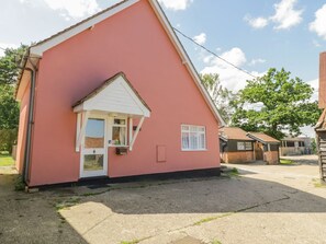 Un bâtiment rose avec une porte blanche, une petite fenêtre et une allée gravillonnée.