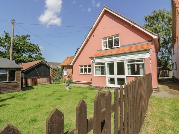 A pink house with a white garage door, a wooden fence, and a grassy yard.