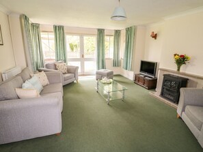 A living room with a sofa, armchair, glass coffee table, television, fireplace, and curtains.