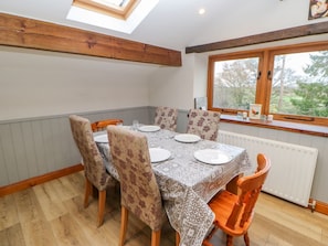 A dining area with a table set for four, wooden chairs, a window with a view of greenery, and a skylight.