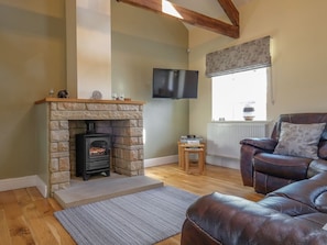 A living room with a stone fireplace, a leather sofa, a television mounted on the wall, and a window with a floral curtain.