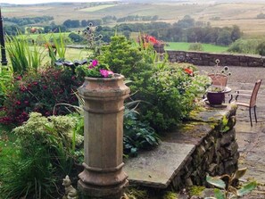 Un jardin avec un pilier en pierre, des plantes en pot et une chaise.