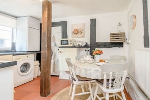 Una cucina con lavatrice, un tavolo e sedie, un termosifone e un orologio appeso al muro.