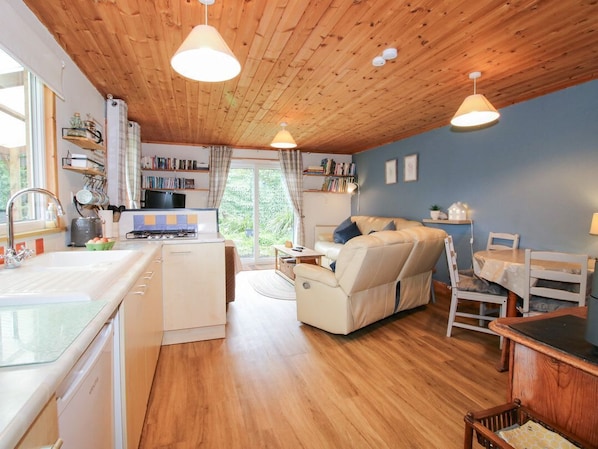 A cozy cabin-style interior with a kitchenette, a sofa, a dining table, and a wooden ceiling.