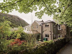 A residential area with houses, a stone wall, and lush greenery. - Cottage on the Green, Gwynedd. (Caernarfon)