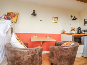 Una habitación con una cama, una mesa de madera, dos sillones marrones, una pequeña zona de cocina con microondas y una pared roja y blanca.