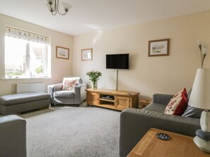 A living room with a grey sofa, a grey armchair, a wooden TV stand, and a flat-screen TV.
