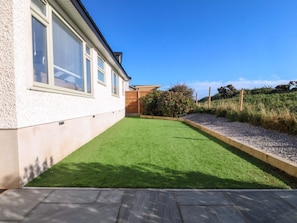 Una casa con un patio empedrado, césped y una valla de madera.