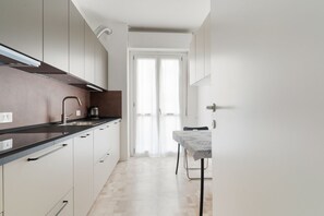 A modern kitchen with white cabinets, a black countertop, and a dining area with a table and chairs. - GuestHost - Modern 58mq apartment for 4 people located on the second floor of a typical Milanese building with lift.The accommodation is located in the De Angeli district, located to the west of the historic center and represented by a quiet atmosphere (Milan)