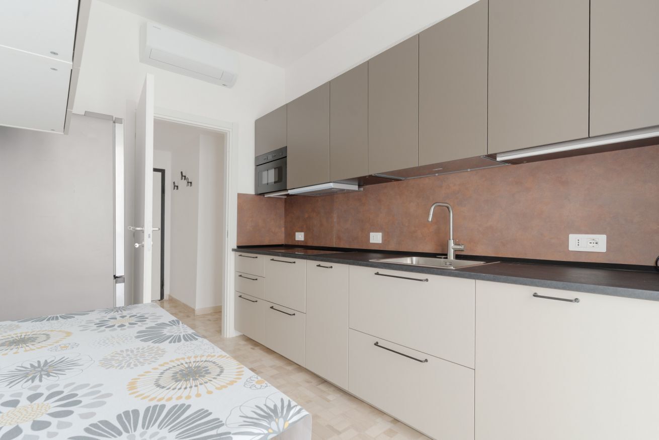 A modern kitchen with grey cabinets, a stainless steel sink, and a built-in oven.