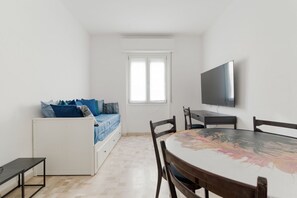Ein gemütlicher Raum mit einem Bett, einem Esstisch, Stühlen, einem an der Wand befestigten Fernseher und einem Fenster.