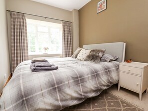 A bedroom with a bed, a nightstand, a window with curtains, and a wall-mounted picture.