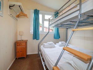 A bunk bed room with a wooden dresser, a window with curtains, and a coat rack with hangers.