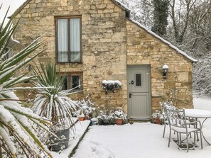 A stone house with a door, window, and a small porch area with chairs and potted plants.