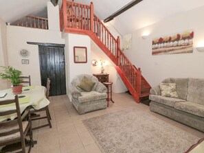 A cozy living room with a staircase, a dining area with a table and chairs, and a sofa.