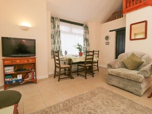 A living room with a television, a dining table with chairs, a sofa, and a bookshelf.