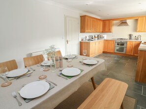 Un comedor con una mesa dispuesta para cuatro personas, armarios de madera, una estufa y un microondas en la cocina.