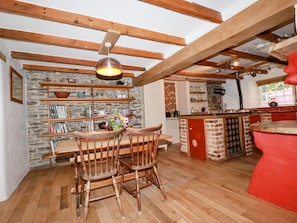 Une cuisine avec des poutres en bois, un mur en pierre, une table à manger avec des chaises et un îlot central rouge.