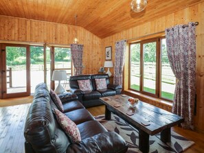 Ein Holzinnenraum mit einem Ledersofa, einem Holztisch und großen Fenstern mit Vorhängen.
