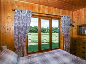 Ein Zimmer mit Holzboden, einem Bett, einem Schminktisch und einem großen Fenster mit Vorhängen.