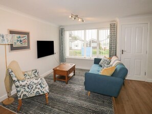 A living room with a sofa, armchair, coffee table, and a flat-screen TV. - Sunny Breeze, Malborough. 2bed (Kingsbridge)