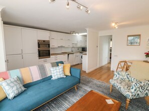 A modern living room with a sofa, a coffee table, and a dining area with chairs. - Sunny Breeze, Malborough. 2bed (Kingsbridge)