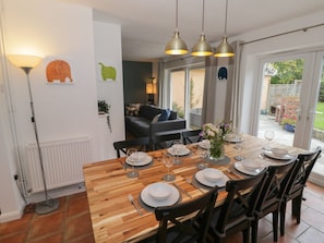 Un coin repas avec une table en bois dressée pour six personnes, une lampe moderne et une vue sur le jardin grâce à des portes vitrées.