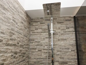 Eine Dusche mit Glasabtrennung, Wandfliesen aus Stein und einem Metall-Duschkopf.