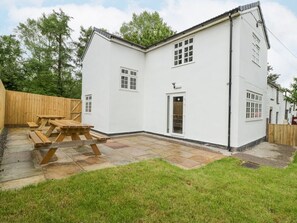 A white two-story house with a patio, a wooden fence, and a wooden table.