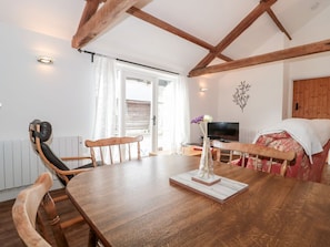Un coin repas avec une table en bois, des chaises, un vase de fleurs, un téléviseur et un lit avec une tête de lit en bois.