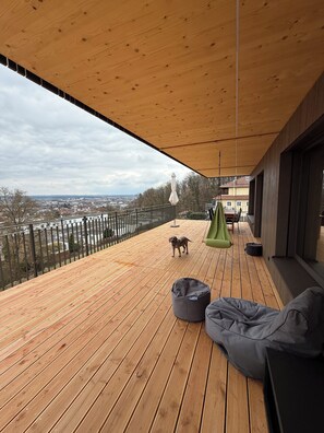 Een houten terras met uitzicht op een stadsbeeld, een hond en tuinmeubilair.