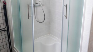 Duschkabine mit Eckausführung, Glastüren, Handbrause und einem Handtuch auf dem Boden.