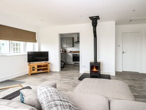 Una sala de estar moderna con un sofá, televisión, chimenea y una cocina visible a través de una puerta abierta.