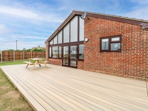 A building with a brick exterior, large windows, and a wooden deck with a picnic table.