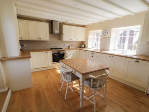 Une cuisine avec un plancher en bois, des armoires blanches, une table à manger en bois et deux chaises blanches.