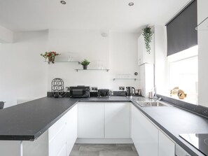 A modern kitchen with white cabinets, a black countertop, and a window with a plant. - Flat 2, 28 Victoria Avenue, Llandudno (Llandudno)