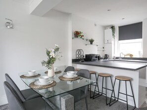 A modern kitchen with a glass dining table, bar stools, and a black countertop. - Flat 2, 28 Victoria Avenue, Llandudno (Llandudno)