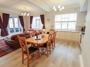 Amplia sala de estar con mesa de comedor, sofá de cuero y área de cocina con armarios y ventana.